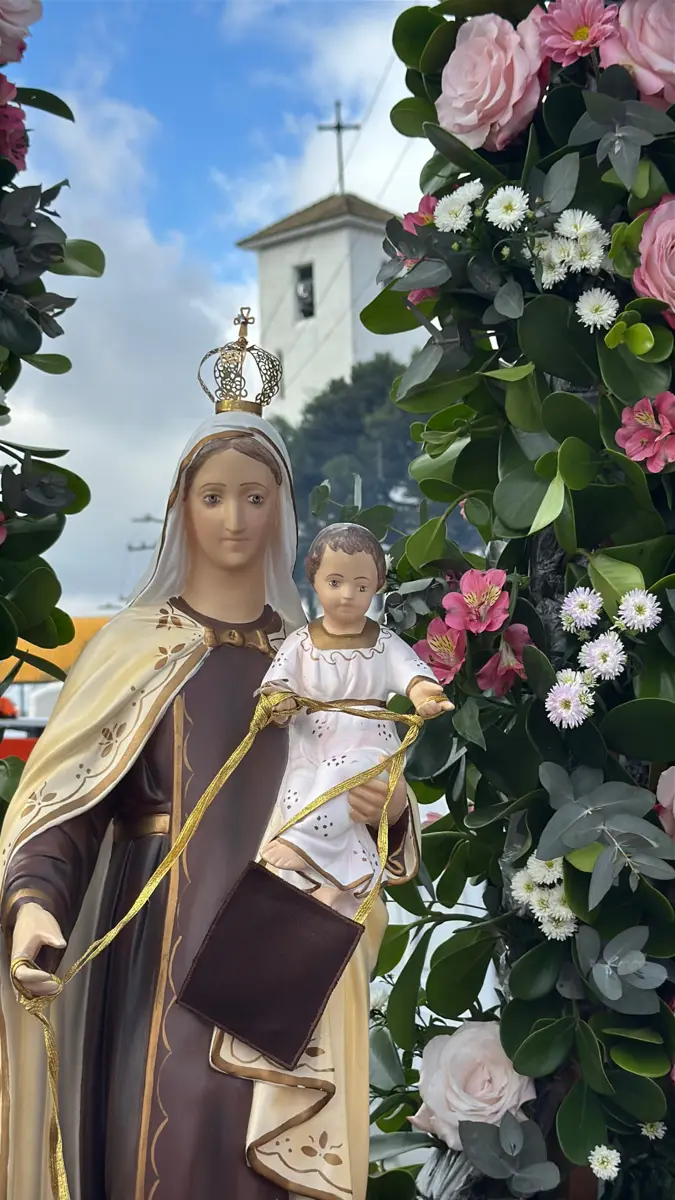 Imagem de Nossa Senhora do Carmo com o Menino Jesus, entre flores, diante das torres do Santuário